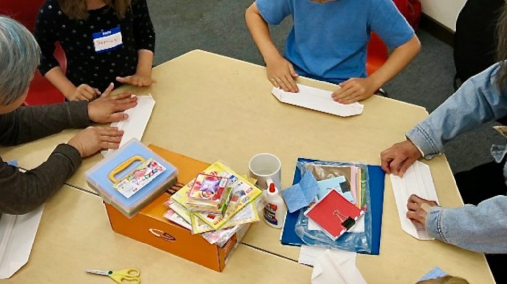 Adults and children at a table folding origami.