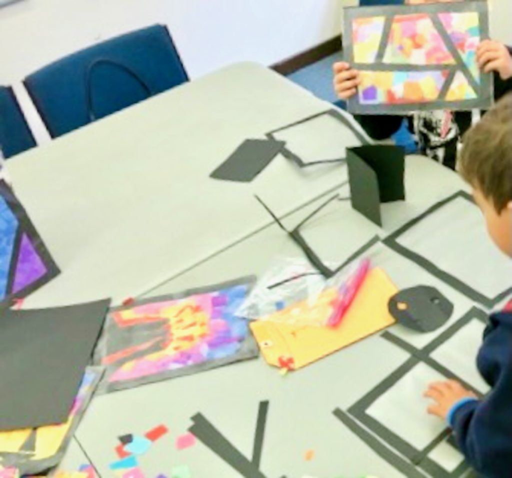 Children sitting at a table working on paper stained glass windows.