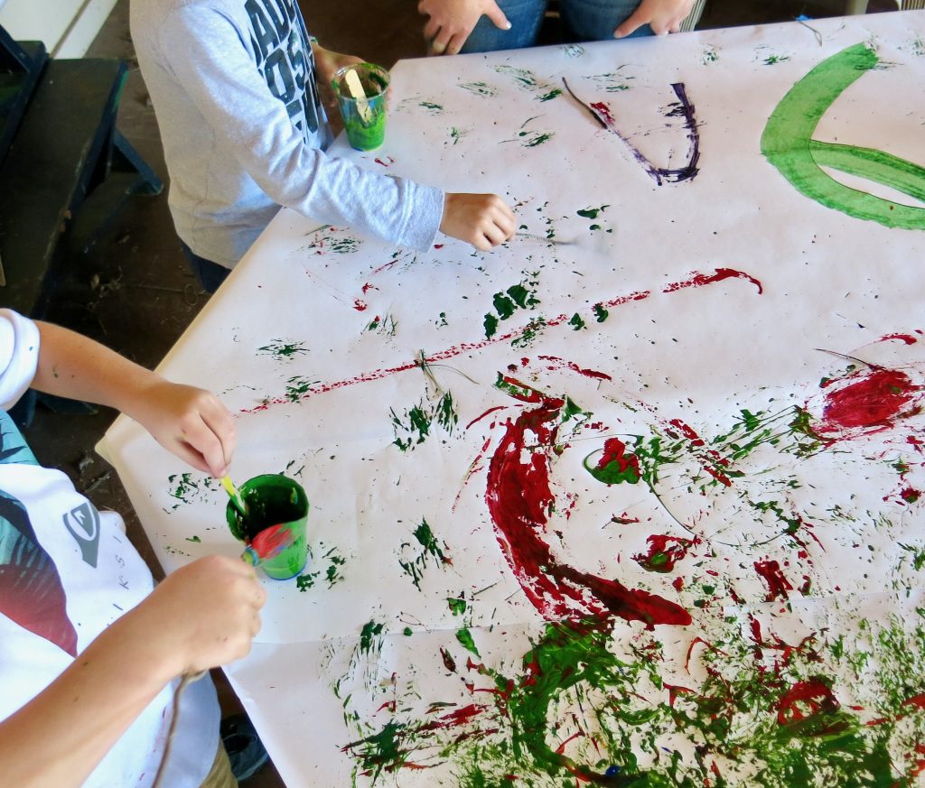 Children's hand wielding natural paint brushes.