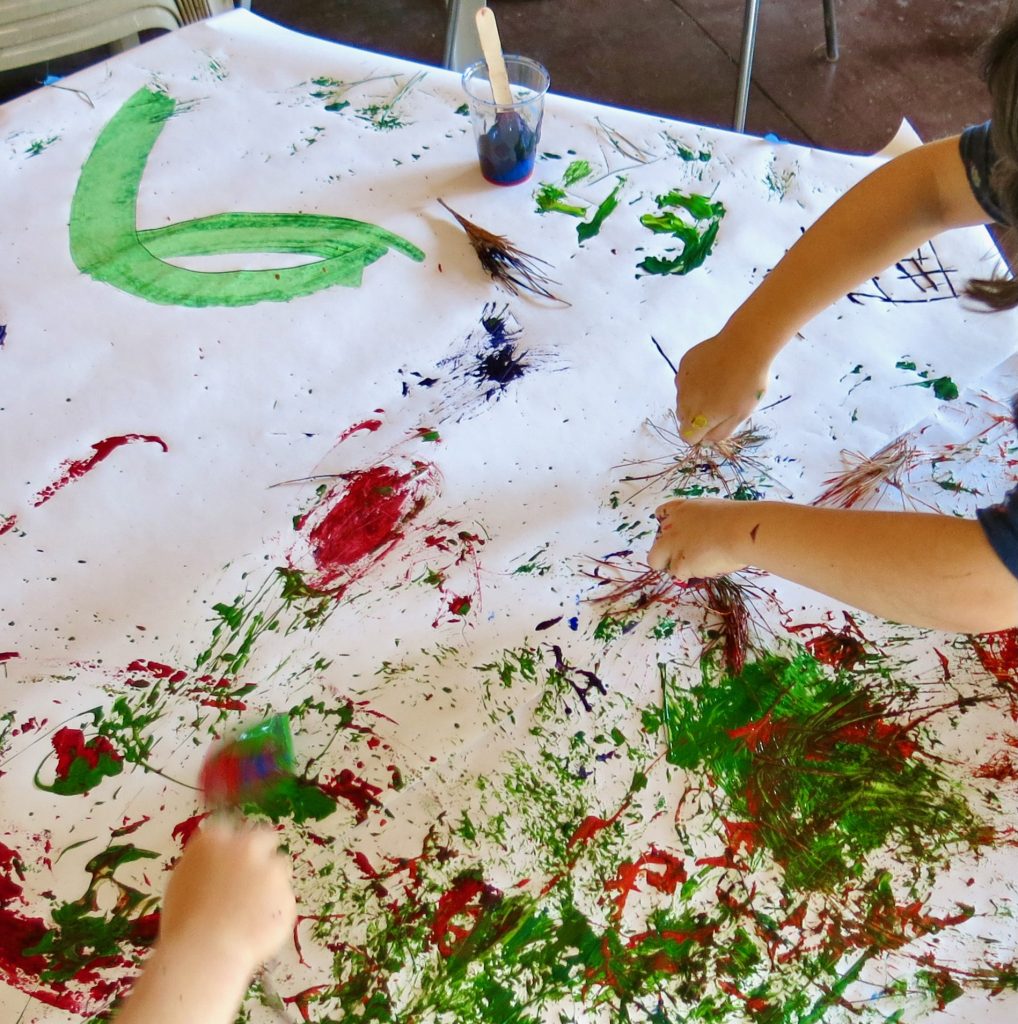 Children's hand wielding natural paint brushes.