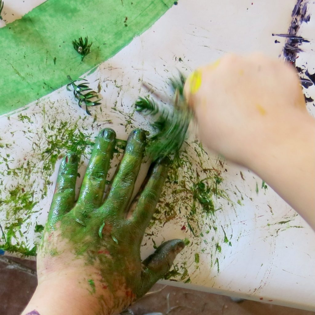 A hand covered in paint wielding a natural paint brush.