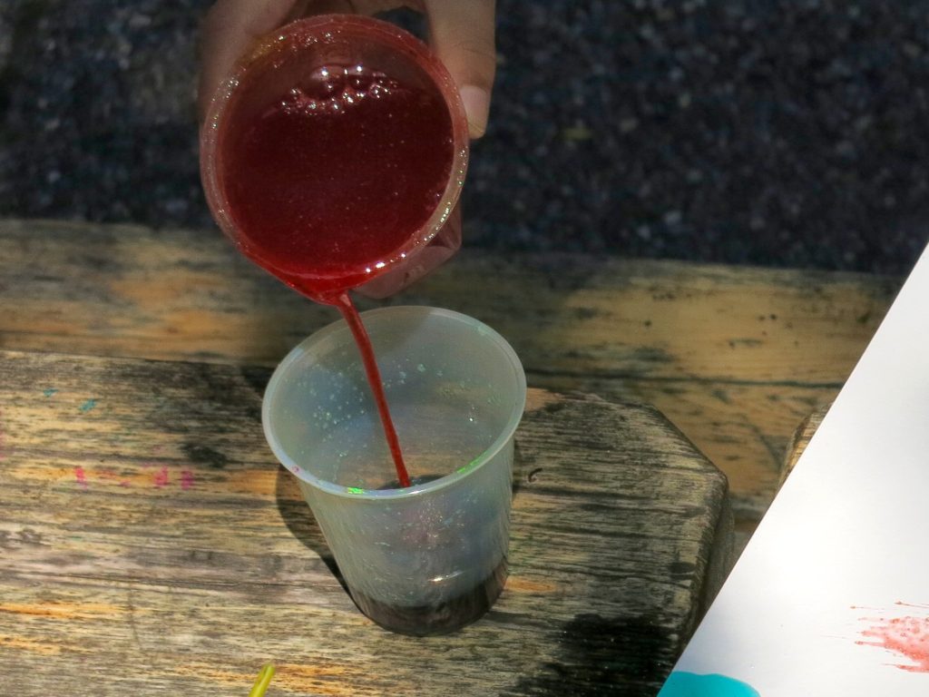 A child's hand pouring a thick liquid from one container into another container.