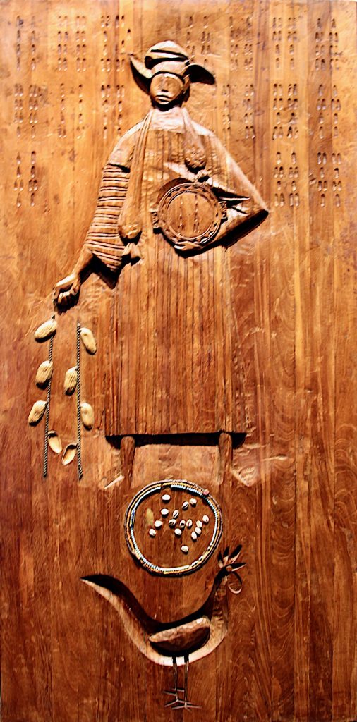 A wooden relief sculpture of a person holding a chain of cowrie shells, with a divination tray at their feet.