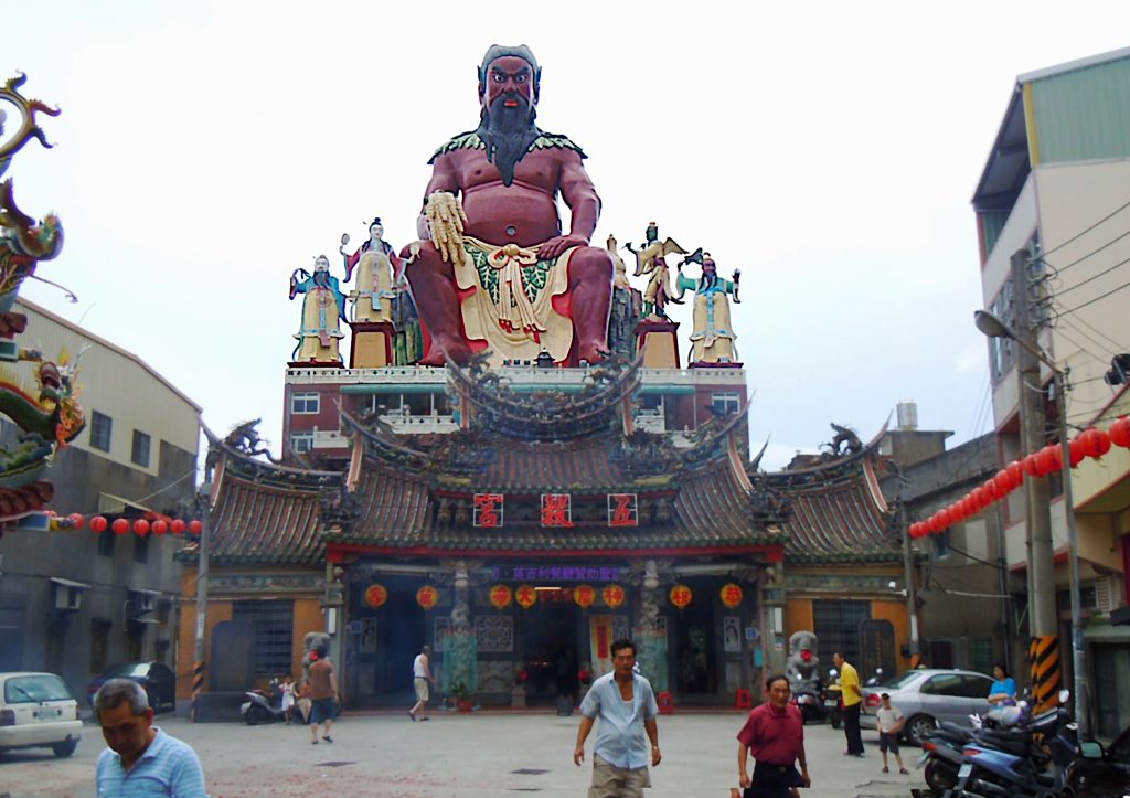 A street scene in China, with a temple and a large statue of Pangu staring down at the camera.