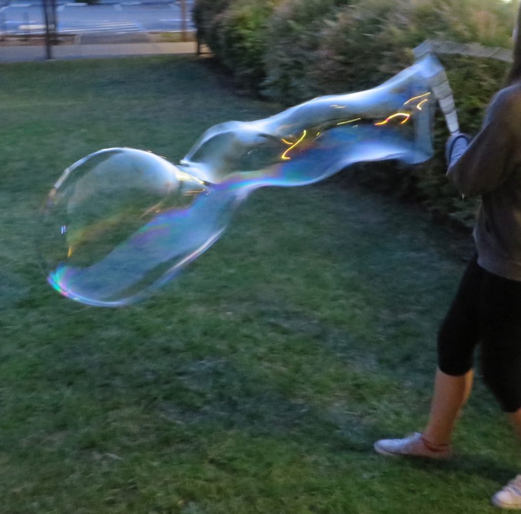 Someone using a tri-string wand to make a giant bubble.