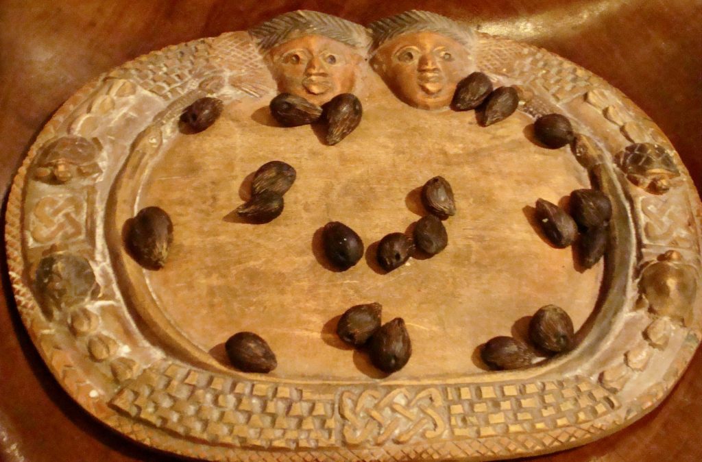 A carved wooden tray with sixteen nuts lying on it.